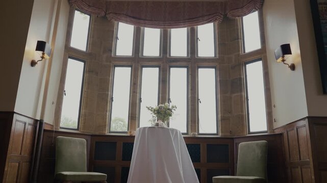 Cinematic interior shot inside an elegant stately home, looking towards a series of large windows overlooking the surrounding grounds and countryside. The camera slowly pans and pulls back to reveal t