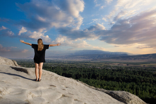 Cheerful happy young child girl standing with arms up on summer mountain outdoors. Adventure success and vacation concept