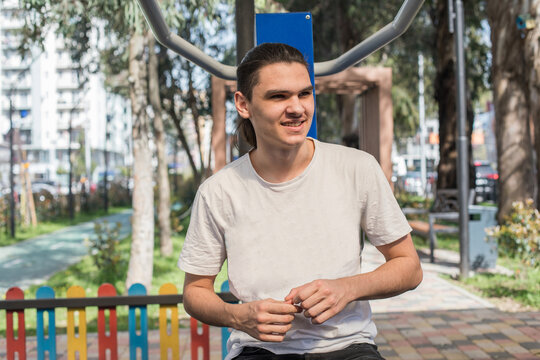 A young man works out in an outdoor gym located in a city park. He uses a pull-up bar to build strength.