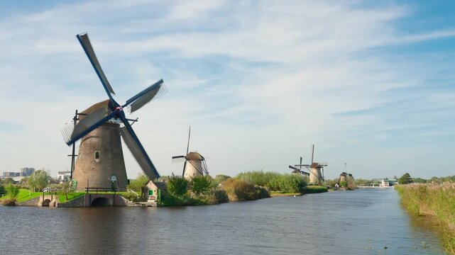 Wide scenic view of the historic windmills of Kinderdijk beside a Dutch waterway, showing the iconic polder landscape and traditional drainage system of the Netherlands.