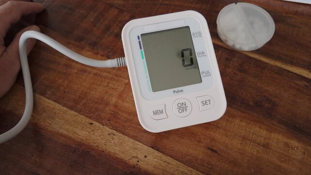 Top-down close-up shows a finger activating a digital blood pressure monitor, illustrating home health technology, diagnostic measurement and routine vital-sign monitoring.