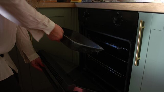 Woman puts tray into electric oven medium 4k shot selective focus