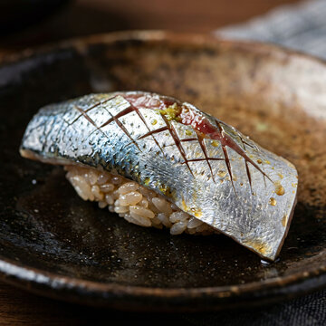 A single piece of fresh kohada gizzard shad nigiri sushi served on a rustic ceramic plate.