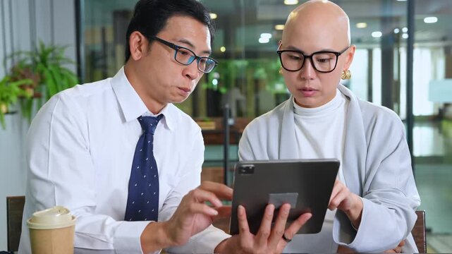 Two business professionals working together in a contemporary cafe using a tablet on a productive workday