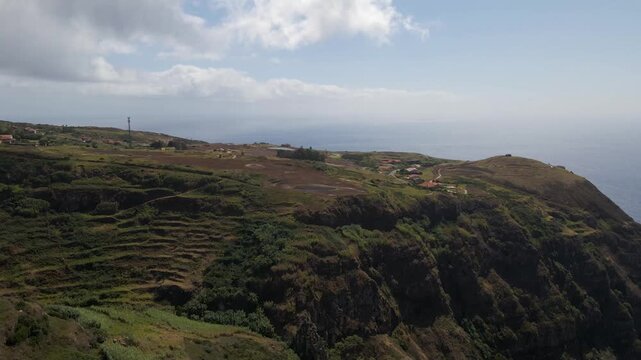 Aerial drone shot sweeping over dramatic cliffs of Ponta do Pargo, revealing a pristine coastal golf course overlooking the Atlantic Ocean. Drone moving backwards away from the golf course.
