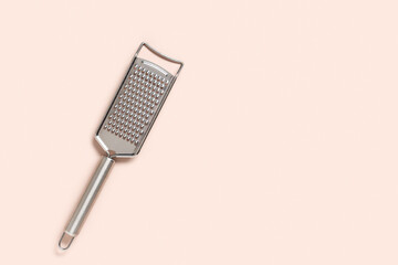 Food preparation and cooking concept, stainless steel kitchen grater for culinary tasks and meal ingredients on a soft pastel pink background © Pixel-Shot