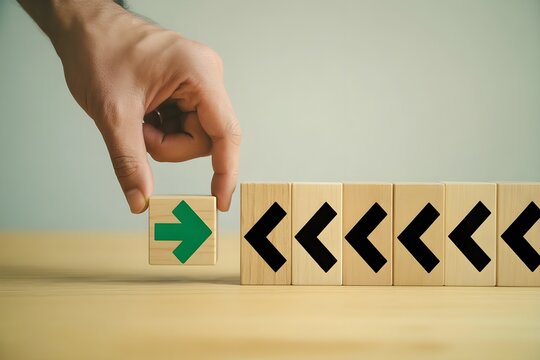 Mano colocando un bloque de madera con una flecha verde orientada en direcci&oacute;n contraria a las dem&aacute;s