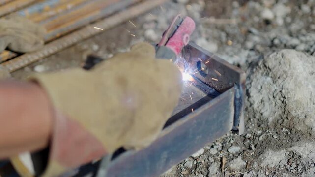 Worker hand in protective glove welds metal details at construction site closeup. Welder uses heating equipment to make carcass in workshop