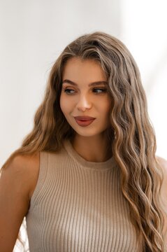 Indoor closeup portrait of woman with wavy brown hair wearing beige ribbed knit sleeveless top with soft natural light and calm expression
