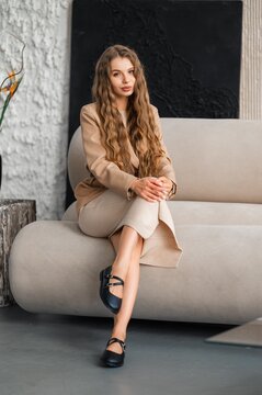 Woman seated on curved beige sofa in modern living room with neutral decor and soft natural light