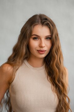 Brunette woman portrait with long wavy hair in beige knit sweater under soft studio lighting, calm confident expression, closeup head and shoulders