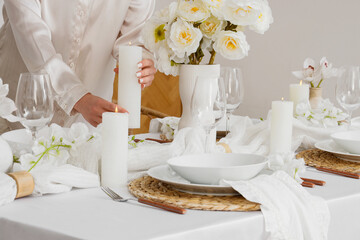 Fototapeta na wymiar Event planning and hospitality, woman setting a table with candles and flowers for a wedding reception or elegant dinner party in a bright room