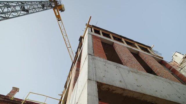 Brick and concrete unfinished building and high tower crane under sky. Urban district infrastructure development at construction site