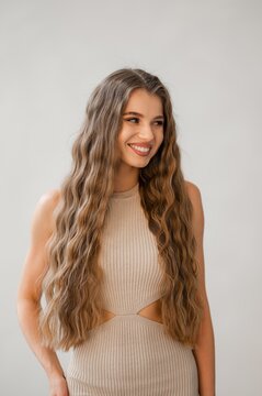 Smiling woman with long wavy hair wearing beige knit top photographed against neutral backdrop showcasing natural glow soft light confident expression casual elegance portrait