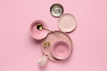 Different plates with bowls, cup and spoon on pink background