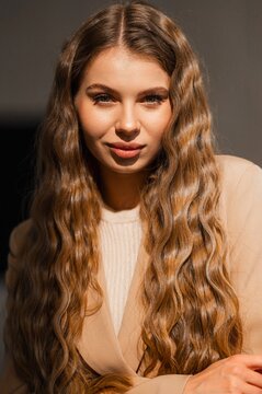 Portrait of woman with long wavy brunette hair under warm lighting, closeup view highlighting clear skin, soft makeup, intimate gaze, and relaxed expression in natural tones