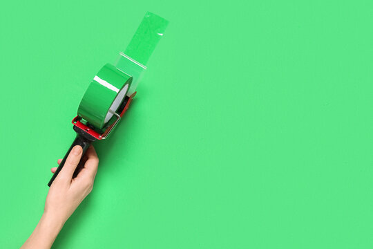 Logistics and shipping efficiency, hand holding a tape dispenser for packaging and parcel preparation on a solid green background