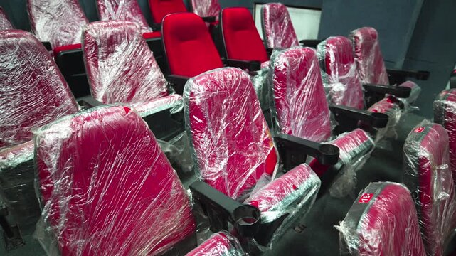 Modern red seats wrapped with plastic foil installed in hall of cinema. Cozy spectator chair lines arranged in auditorium of movie theater