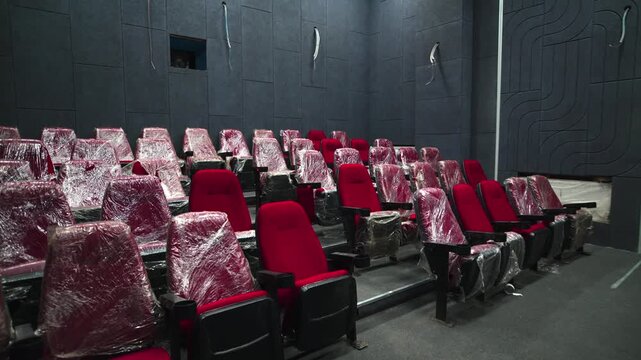 Soft red seats wrapped with plastic foil in hall of modern cinema. Comfortable chair rows for spectators inside incomplete movie theater