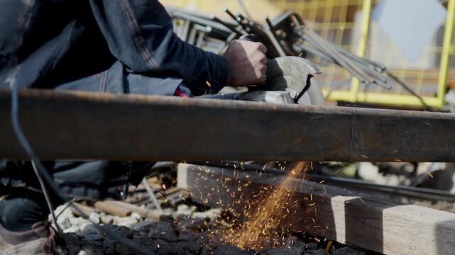 Builder with disk saw cuts hollow structural section in parts at construction site closeup. Man worker prepares metal beam details outdoors