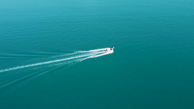 Fast fishing boat moving across the sea, aerial drone view. Speed boat sailing on the open ocean water. Drone footage of a fishing vessel leaving a wake in the sea.
