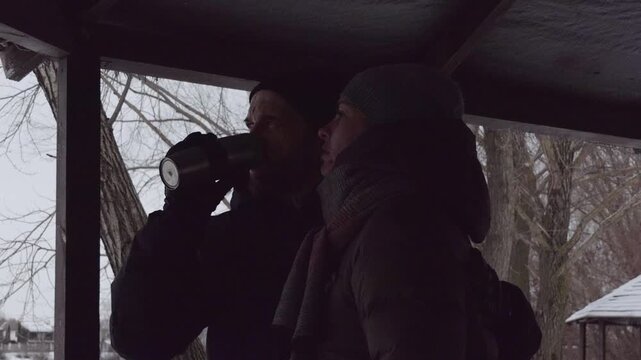 Loving couple resting outdoors on a cold winter day, drinking warm tea from a thermos