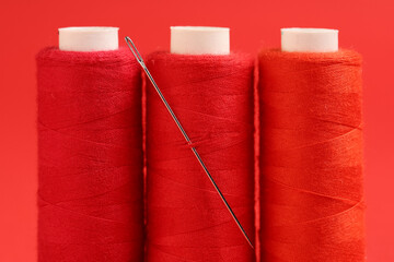 Spools of thread with needle on red background, closeup