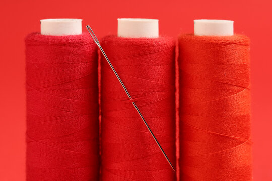 Spools of thread with needle on red background, closeup