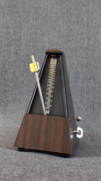 Vintage wooden mechanical metronome ticking at a steady tempo and gradually slowing down until it stops. Rhythm, timing, music practice, time measurement, countdown, patience, discipline.