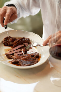 Man Cutting Juicy Beef Steak with Glass of Red Wine in Restaurant