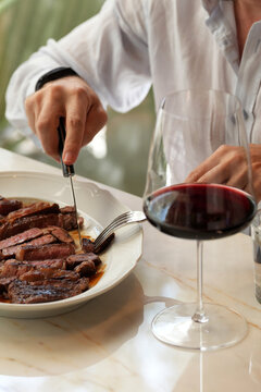 Man Cutting Juicy Beef Steak with Glass of Red Wine in Restaurant