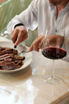Man Cutting Juicy Beef Steak with Glass of Red Wine in Restaurant