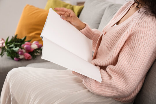 Young woman reading blank magazine at home on spring day, closeup