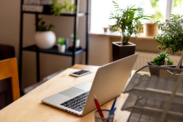 Fototapeta premium Cozy work from home setup with laptop and indoor plants - minimalist home office, productivity and flexible work lifestyle