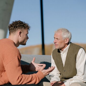 Young and elderly man deep conversation face to face sitting for community program poster and intergenerational support campaign background