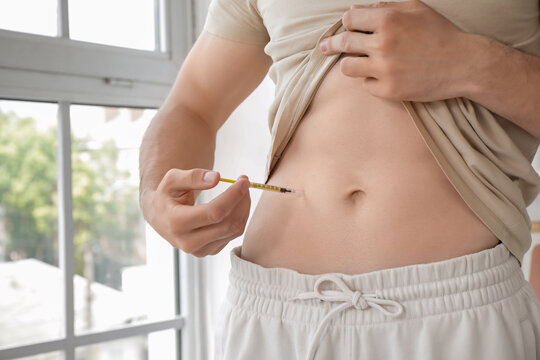 Diabetic young man giving himself insulin injection at home, closeup