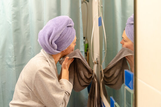 Woman wiping her face with a towel in front of the bathroom mirror after a shower