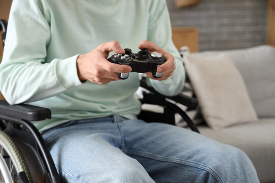 Young man in wheelchair playing video game at home, closeup