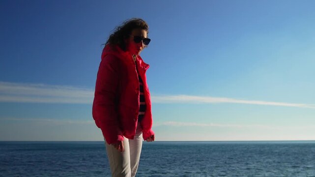 Woman ocean jacket standing by the blue sea on a sunny winter day enjoying the fresh breeze and coastal view