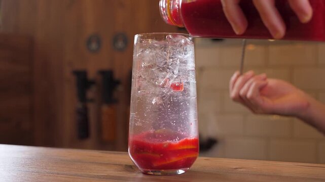Close-up of the bartender pouring berry syrup into lemonade with ice and berry juice at the bar. Slow motion. The process of making cooling berry lemonade.