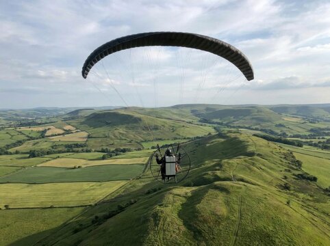 Paramotor pilot soaring over lush green ridges with electric battery
