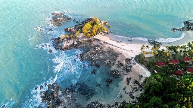 drone hover footage of a tropical island featuring turquoise water, rocky shoreline, sandy beach, palm trees, and peaceful coastal scenery in a serene seaside setting