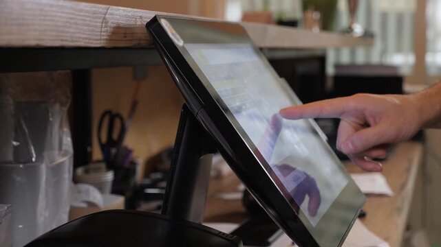 A close-up of a waiter or bartender working at a computer in a cafe. He swipes a card through the terminal and places an order. The waiter holds a card in his hand, selects a table on the touch screen
