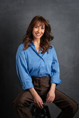 Confident mature Woman ins blue shirt sitting against isolated background