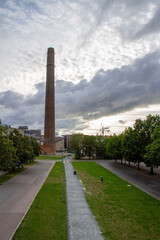 Fototapeta premium The historic brick chimney of Kultuurikatel framed by a linear grass path perspective, filmed from Linnahall terraces under a dramatic cloudy sky in Tallinn, Estonia.