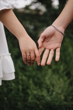 Close-up wedding photo of newlyweds, bride and groom holding hands outdoors.