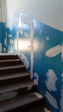 Plastered holes and repaired wall damage on a stair landing inside a residential building, representing entrance renovation, wall leveling, plastering and repair work.