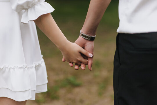 Close-up wedding photo of newlyweds, bride and groom holding hands outdoors.