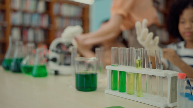 A table filled with glass beakers and test tubes of green liquid in a library science lesson
