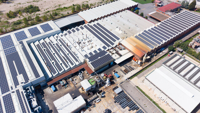 Aerial view of an industrial facility producing fasteners, screws, and bolts, featuring extensive rooftop solar panel arrays and metal materials stored in the yard in Cornaredo, Lombardy, Italy.
